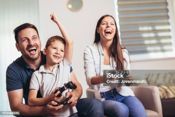 Uśmiechnięta Rodzina Siedząca Razem Na Kanapie Grając W Gry Wideo - zdjęcia stockowe i więcej obrazów Gra wideo