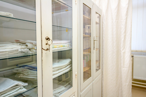 Stacks of clean tidy bed sheets and towels are placed in shelves at storage room with old white cabinets.