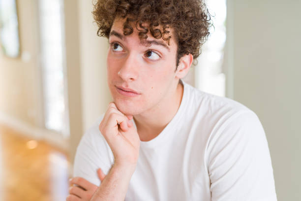 istock Young handsome man wearing white t-shirt with hand on chin thinking about question, pensive expression. Smiling with thoughtful face. Doubt concept. 1175470246
