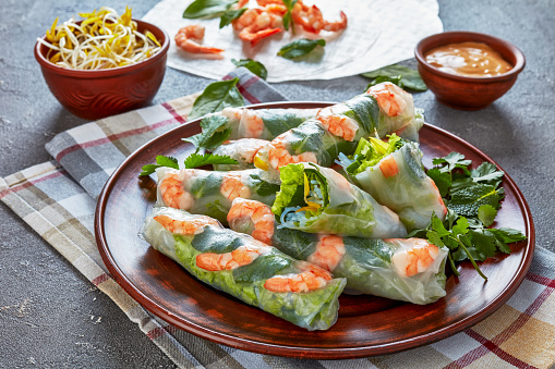 Asian spring rolls of rice paper with shrimps, rice noodle, spinach, mung bean sprouts fillings on an earthenware plate, horizontal view from above