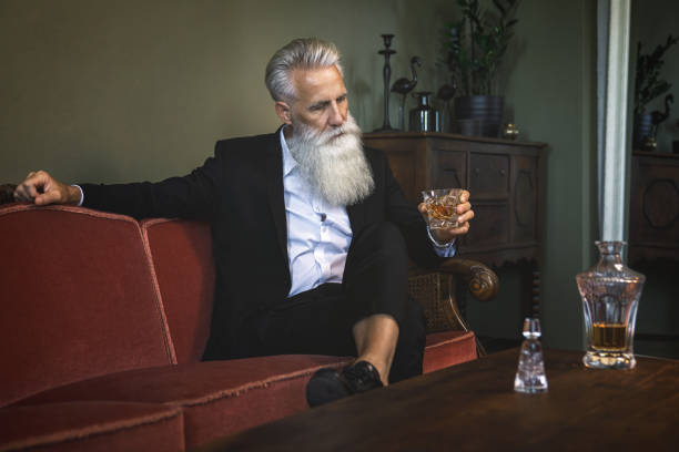 schöne bärtige senior mann trinken whisky - smoking issues fotos stock-fotos und bilder