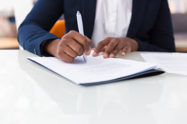 Businesswoman signing contract Businesswoman signing contract. African American business woman sitting at table in office, holding pen and writing in document. Legal expertise concept endorsing photos stock pictures, royalty-free photos & images