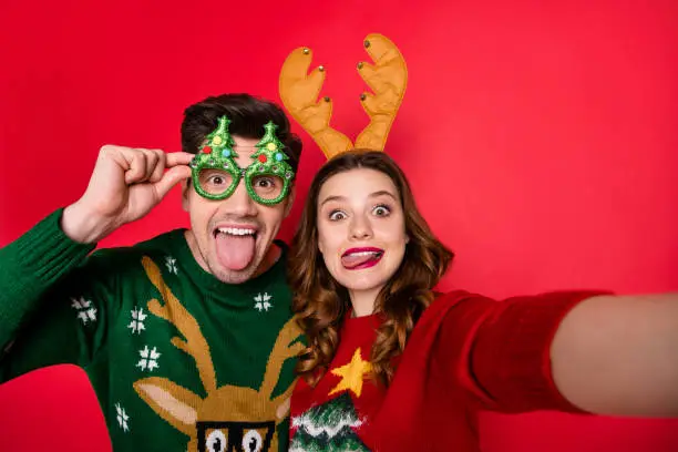 Photo of Photo of childish lady and guy at x-mas costume party making selfies wear ugly knitted pullovers isolated red color background