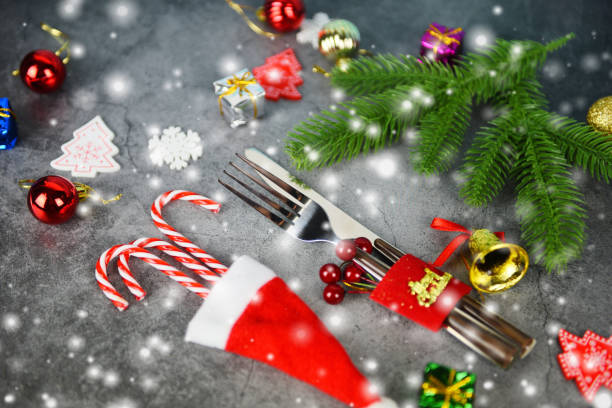 Christmas table place setting decoration gift box ball candy cane in santa claus hat fork and knife Xmas New Year food lunch festive Christmas dinner holidays background themed party with snow