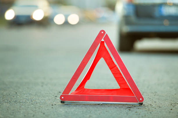istock Red emergency triangle stop sign and broken car on a city street. 1175475625