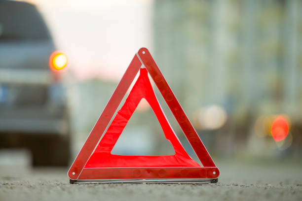 istock Red emergency triangle stop sign and broken car on a city street. 1175475631