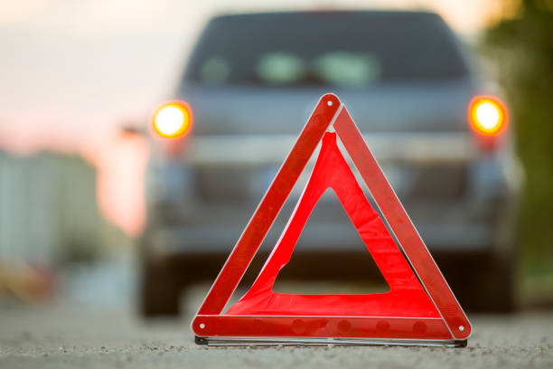 istock Red emergency triangle stop sign and broken car on a city street. 1175475641