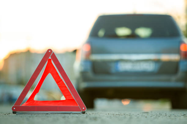 istock Red emergency triangle stop sign and broken car on a city street. 1175475662
