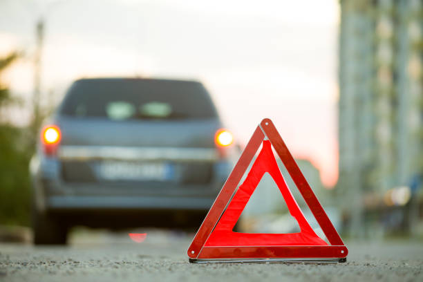 istock Red emergency triangle stop sign and broken car on a city street. 1175475669
