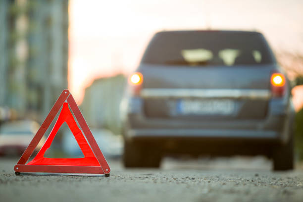 istock Red emergency triangle stop sign and broken car on a city street. 1175475682