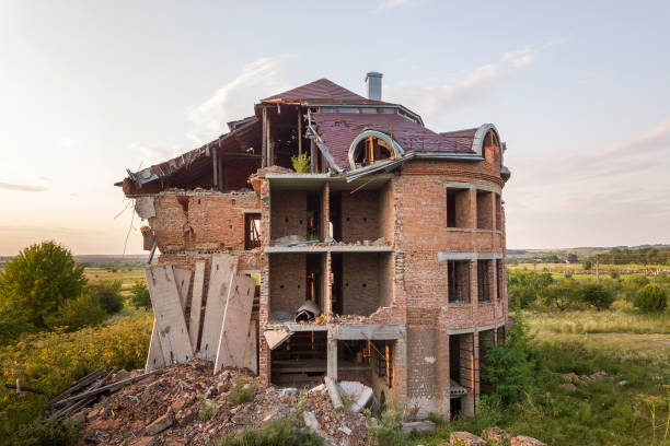 Dismantling a house more than 100 years old. Facade still remaining. Background hydraulic lift and excavator. Front heap of broken bricks laying on ground from demolition