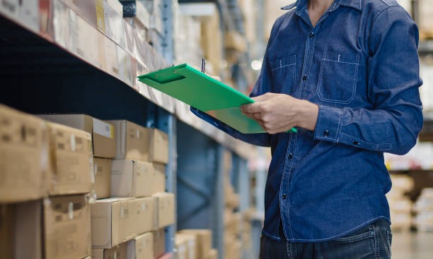 asian manager man doing stocktaking of products management in cardboard box on shelves in warehouse using clipboard file and pen. male professional assistant checking stock in factory. physical inventory count. - department store imagens e fotografias de stock