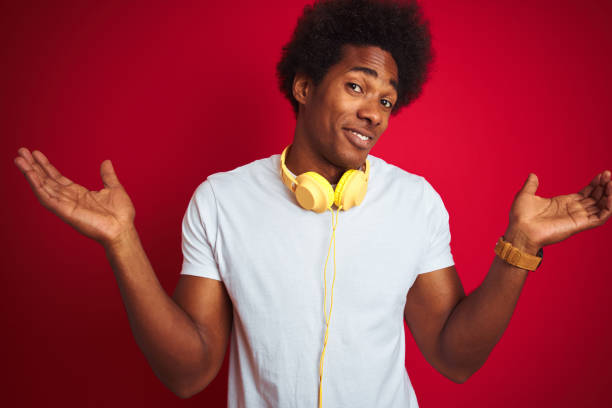young african american man listening to music using headphones over isolated red background clueless and confused expression with arms and hands raised. doubt concept. - head and shoulders audio imagens e fotografias de stock