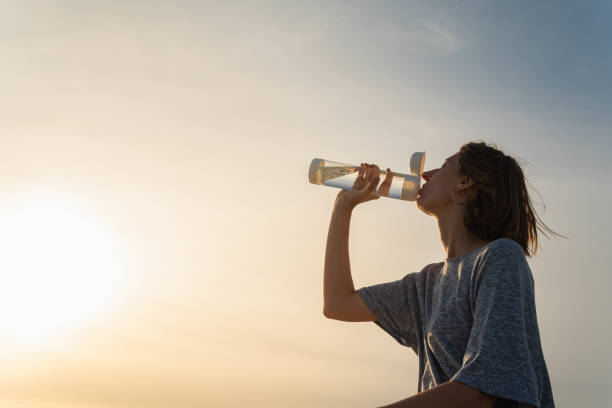 istock Young woman drinks water from a bottle on a sunset sky background. 1175481650