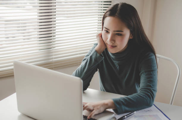 istock pretty young asian woman typing working and using laptop and document on desk at home office, lifestyle, searching web, social network, online, finance, investment and digital technology concept 1175482010