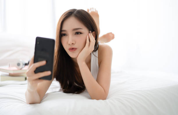 istock Beautiful young Asian woman making selfie using a smartphone and smiling while lying on bed. People addiction to new technology trends. 1175485682