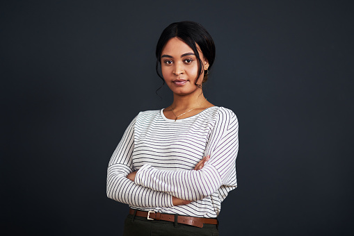 Cropped portrait of an attractive young businesswoman standing alone with her arms folded against a black background in the studio