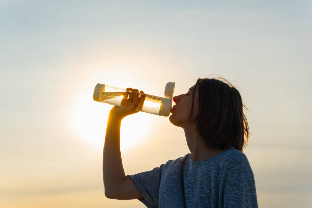 istock Young woman drinks water from a bottle on a sunset sky background. 1175488893
