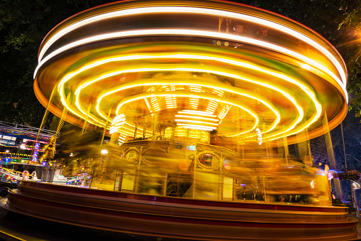 The bright lights of a fast moving fairground merry-go-round blur against a dark night sky. The motion blurred yellow lights are spinning underneath the rides carousel.