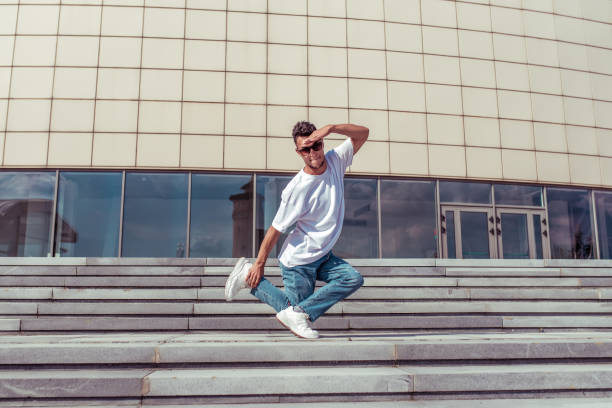 dancer in the summer in the city, dancing break dance, bottom style, free space, jeans t-shirt sneakers, sunglasses, active movement in the jump stock photo