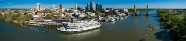 Photo of Steamboat at the pier in Old Sacramento Waterfront District, with the remote view of Tower Bridge, Historic district, and Sacramento Downtown, in the backdrop. Aerial drone stitched XXXL high-resolution panorama.