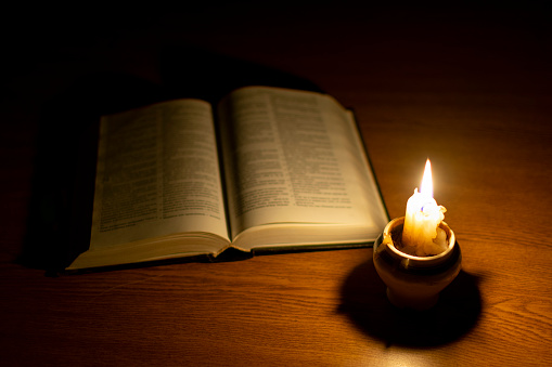 an old book opened for reading and a candle on the table that illuminates the darkness around