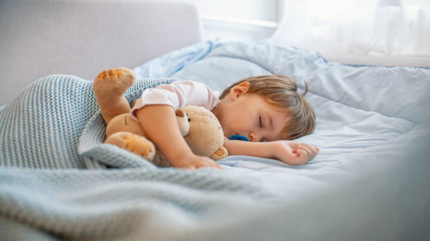 istock Adorable kid boy after sleeping in grey bed with toy 1175497481
