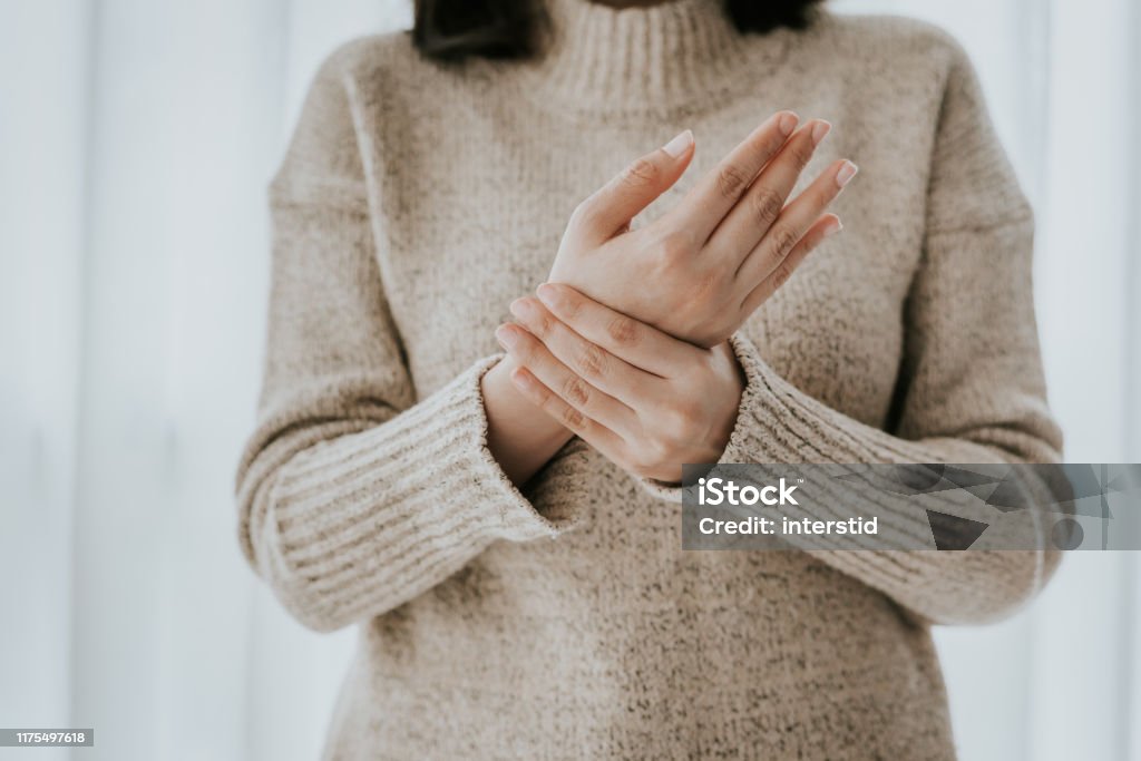 Woman suffering from wrist pain Cropped shot of woman in sweater holding her wrist pain Pain Stock Photo