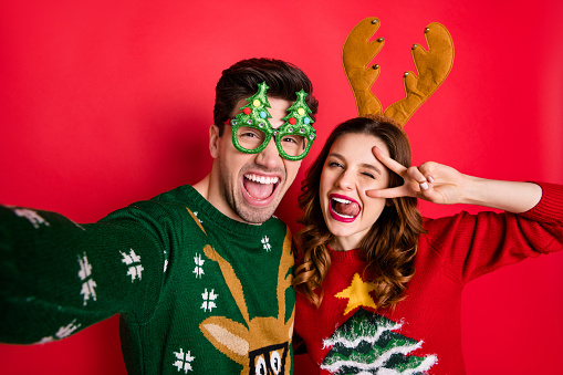 Foto de pareja loca haciendo selfies pegando lenguas guiñando los ojos v-firma usar funky feoadors jumpers aislados de color rojo fondo photo