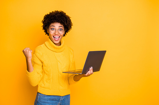 Portrait of her she nice attractive lovely charming smart clever cheerful wavy-haired girl holding in hands laptop celebrating winning, isolated over bright vivid shine vibrant yellow color background