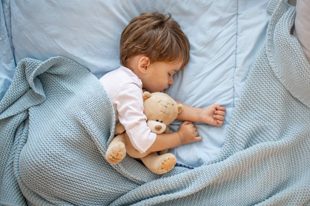 фотография мальчика, спящего вместе с плюшевым мишкой. - baby lying down indoors one person стоковые фото и изображения