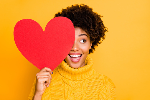 Photo of trendy cheerful cute nice charming curly fascinating girlfriend looking out away from red big heart wearing yellow jumper, while isolated with bright color background