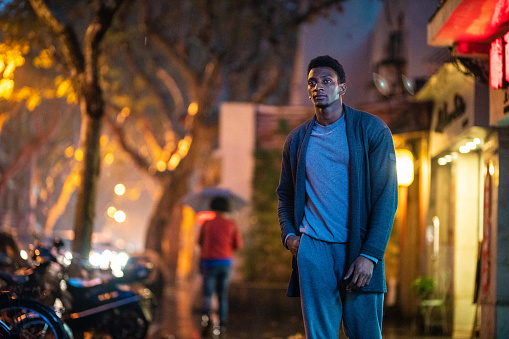 Portrait of young, handsome African man with hands in pocket on city streets at night