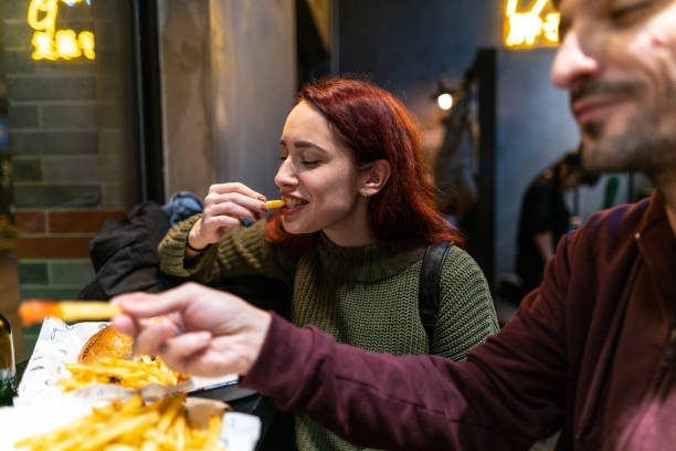 Hungry couple in fast food restaurant Young hungry couple eating yummy hamburgers and french fries  in fast food restaurant, laughing and having fun dyed red hair photos stock pictures, royalty-free photos & images