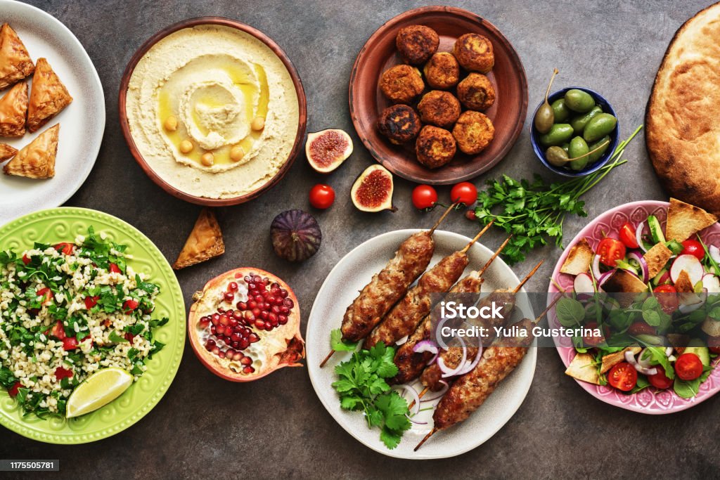 Tavolo da pranzo arabo e mediorientale. Hummus, insalata tabbouleh, insalata Fattoush, pita, kebab di carne, falafel, baklava, melograno. Set di piatti arabi. Vista dall'alto, lay piatto - Foto stock royalty-free di Cibo