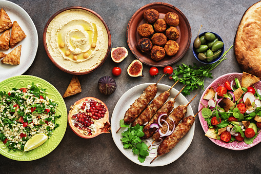 Arabic and Middle Eastern dinner table. Hummus, tabbouleh salad, Fattoush salad, pita, meat kebab, falafel, baklava, pomegranate. Set of Arabian dishes.Top view, flat lay.