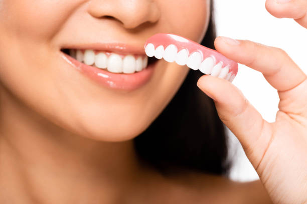 istock cropped view of woman holding false teeth isolated on white 1175507063