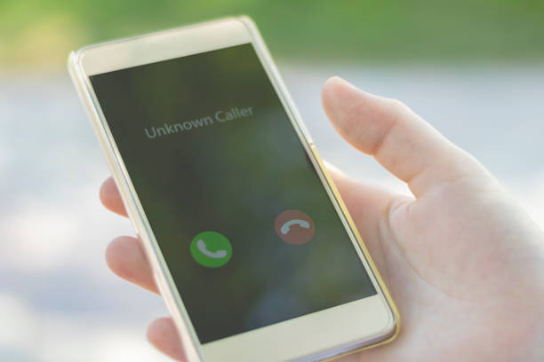 Unknown caller. A woman holds a phone in his hand outdoors in a park and thinks to end the call. Incoming from an unknown number. Incognito or anonymous stock photo