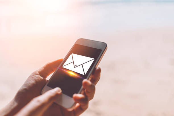 Woman hand using smartphone at sunset beach with email icon background. Technology business and travel freedom concept.