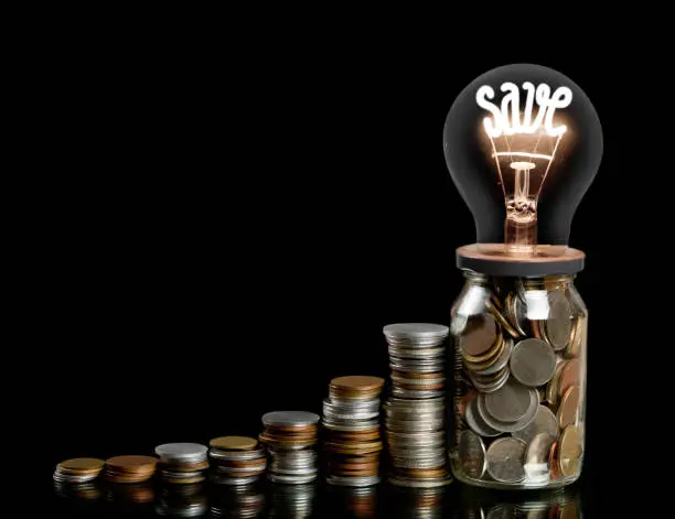 Group of coin rows, glass jar and light bulb with shining fiber in a shape of SAVE concept word isolated on black background