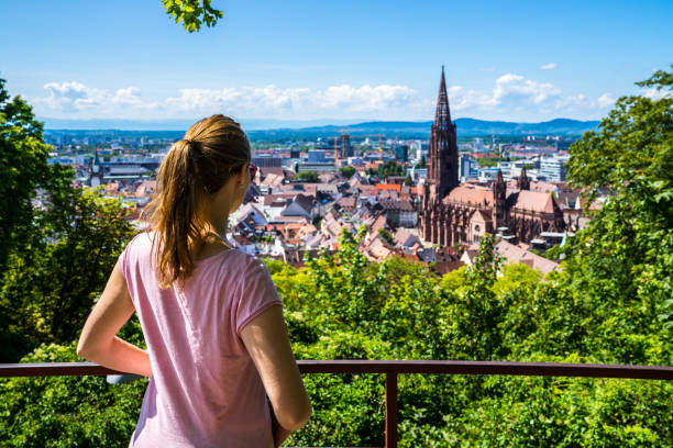 Germany, Stunning blonde woman with ponytail enjoying view above city freiburg im breisgau and skyline with famous muenster cathedral in summer vacation stock photo