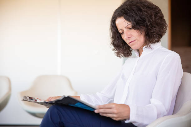istock Serious female office worker reading magazine 1175512889