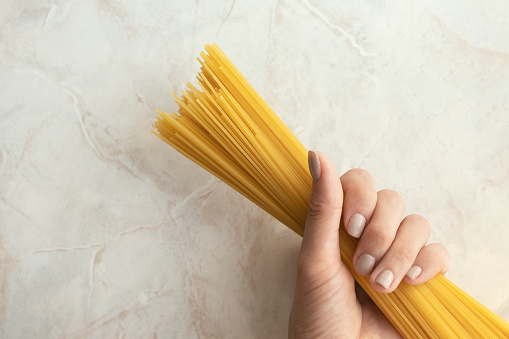 Woman holding long spaghetti ready to cook. Ingredient for Italian pasta. Raw food, close-up