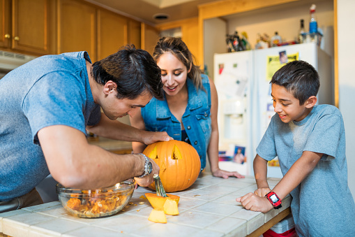 Hispanic US family carving pumpkin together. Mother, Father and Son