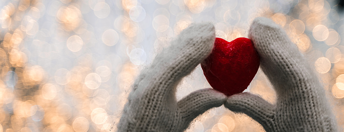 Female hands in knitted white mittens with heart of snow in winter day. Love and St. Valentine cozy concept, copyspace, bokeh background, banner