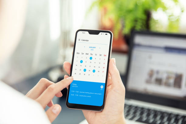 a mulher de negócios aponta a tela do smartphone e verific o calendário na aplicação. aplicação na tela criada no programa gráfico - personal organizer - fotografias e filmes do acervo