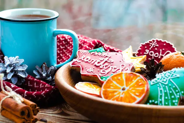 Christmas card: A cup of hot tea stands on a wooden table next to a wooden plate on which are gingerbread cookies made from orange slices against the background of a window with water drops