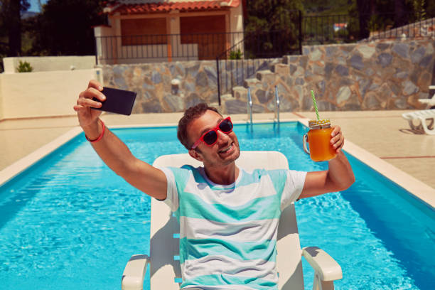 istock Attractive man using cellphone while drinking juice near swimming pool. 1175534224