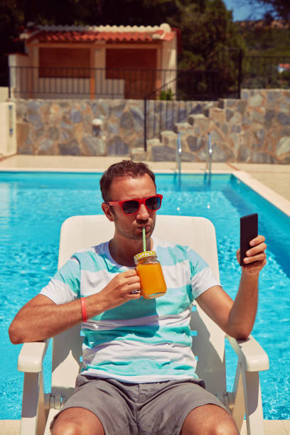 istock Attractive man using cellphone while drinking juice near swimming pool. 1175534281