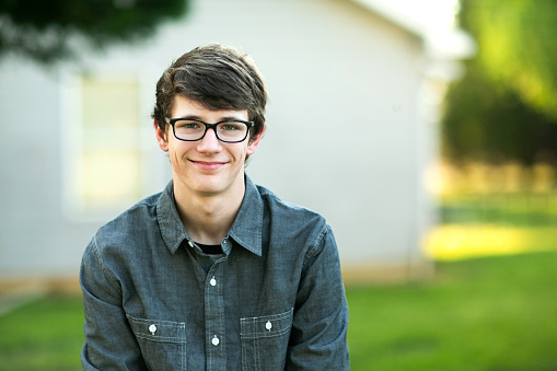 Teenage boy with glasses wearing a gray shirt and denim jeans sitting outside